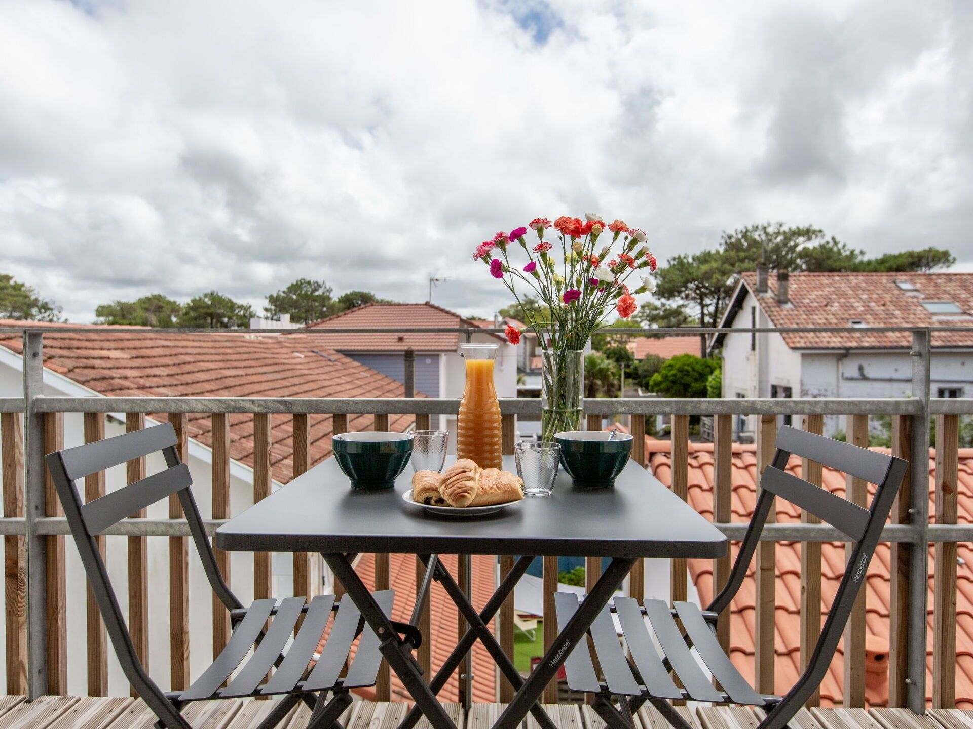 Ein Balkon mit einem Frühstückstisch, komplett mit Croissants, einem Glas Orangensaft und einer Blumenvase.