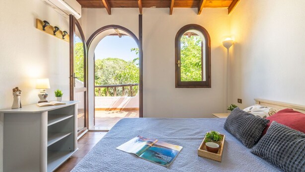 Ein Schlafzimmer mit einem Bett, einem Nachttisch mit Lampe, einem kleinen Regal und einem Fenster.