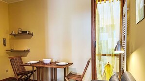 A dining area with a wooden table set for four, two chairs, and a sofa in the foreground. - Lovely apartment for 3 guests with pool, TV, balcony and pets allowed (Cipressa)