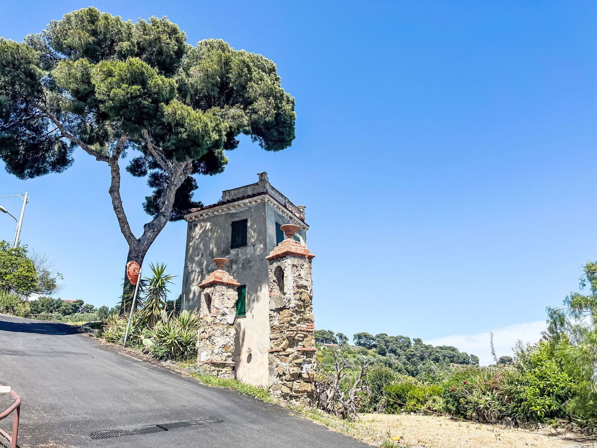 Un edificio de piedra con una pequeña torre, rodeado de vegetación y árboles.