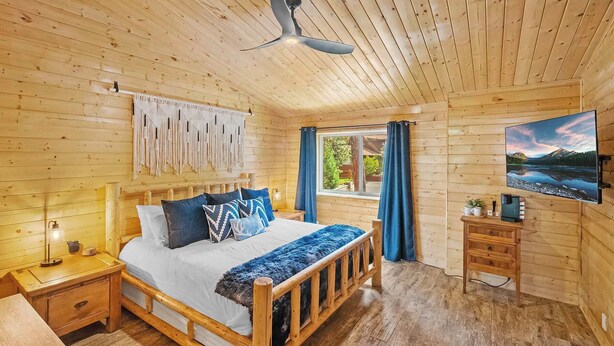 Un dormitorio de cabaña de madera con una cama, mesita de noche, lámpara y televisor sobre un tocador.