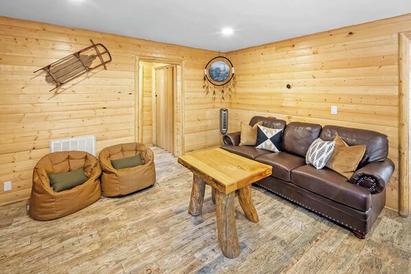 A cozy room with a wooden interior, a leather sofa, two bean bags, and a wooden coffee table.