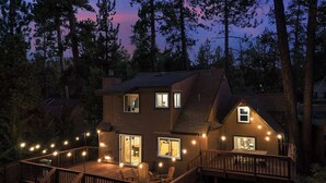 Una casa de dos pisos con un balcón, luces de cadena y vistas del bosque circundante.