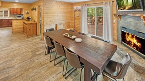 Un interior de cabaña acogedor con una mesa de comedor de madera, sillas, una zona de cocina y una chimenea.