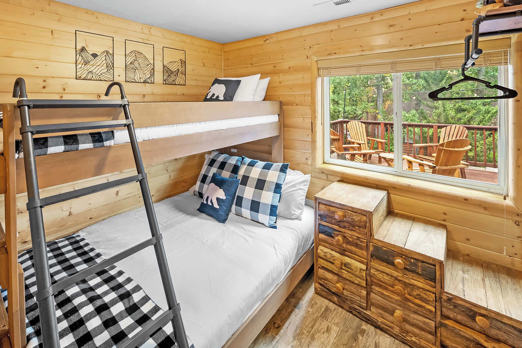 Une chambre avec des lits superposés, donnant sur l’extérieur, avec une commode en bois et une fenêtre donnant sur une terrasse.