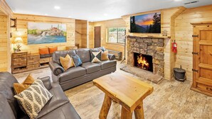 Acogedor interior de una cabaña de madera con chimenea de piedra, un sofá de cuero y una mesa de centro de madera.