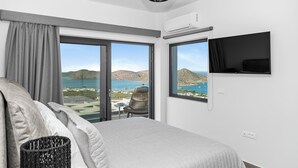 A bedroom with a bed, a TV, a window with a view of the sea, and a chair by the window.