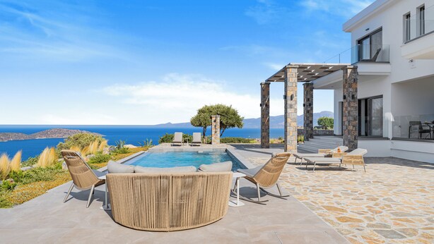 A pool area with lounge chairs and a pergola, overlooking a scenic view of the sea and mountains.