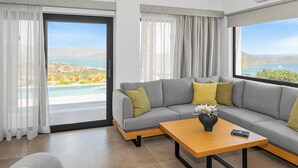 A modern living room with a grey sectional sofa, a wooden coffee table, and a view of a pool and hills.