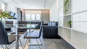 A modern kitchen with a glass dining table, black chairs, a black sofa, and a white cabinet with plants.