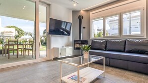 A modern living room with a glass coffee table, a black leather sofa, a flat-screen TV, and a fireplace.