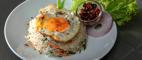 Un plato de arroz frito coronado con un huevo estrellado, acompañado de un tazón pequeño de salsa de chile rojo, lechuga y una rodaja de cebolla roja.