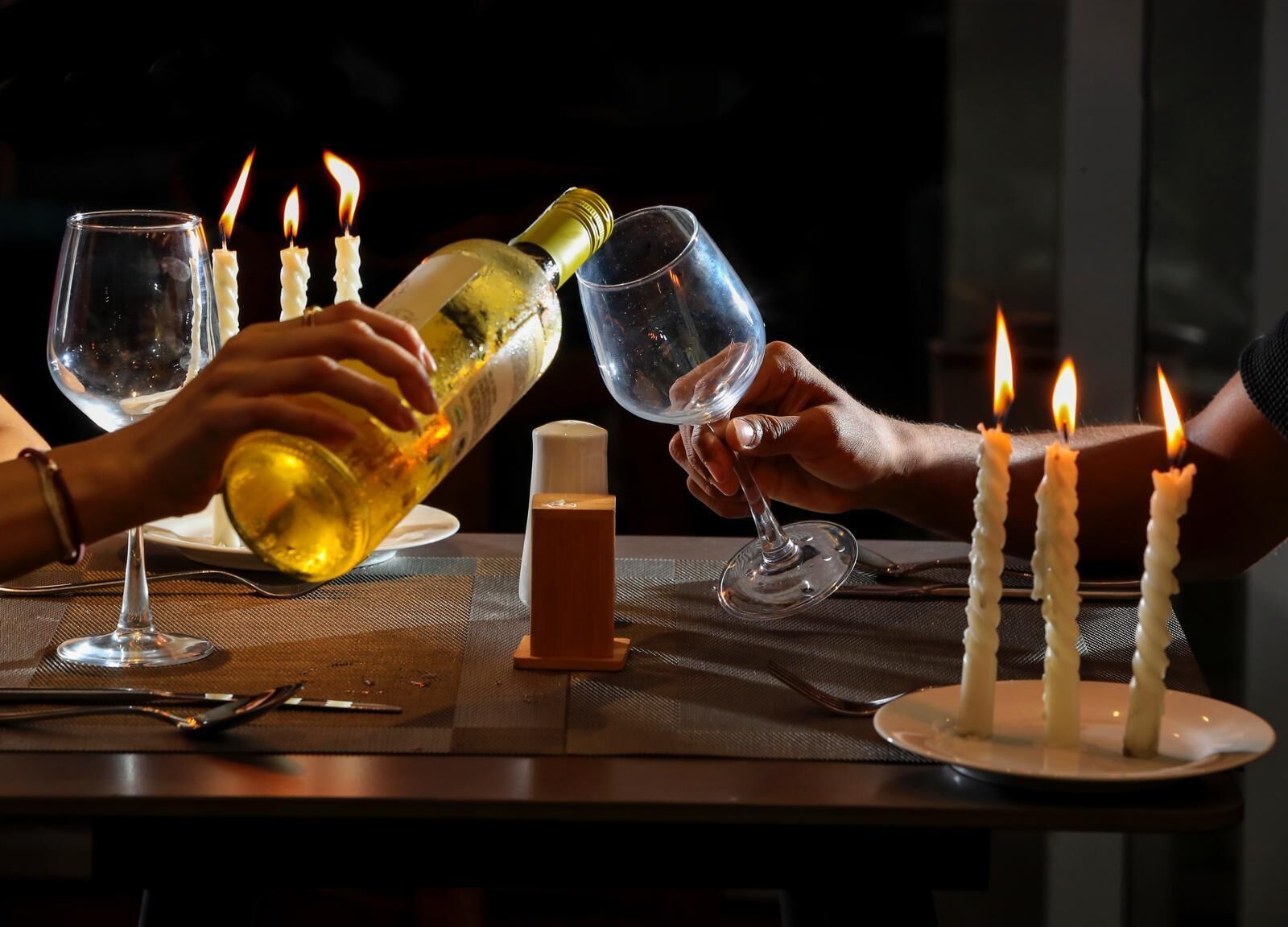 Taula de menjador amb copes de vi, ampolla de vi i espelmes enceses.