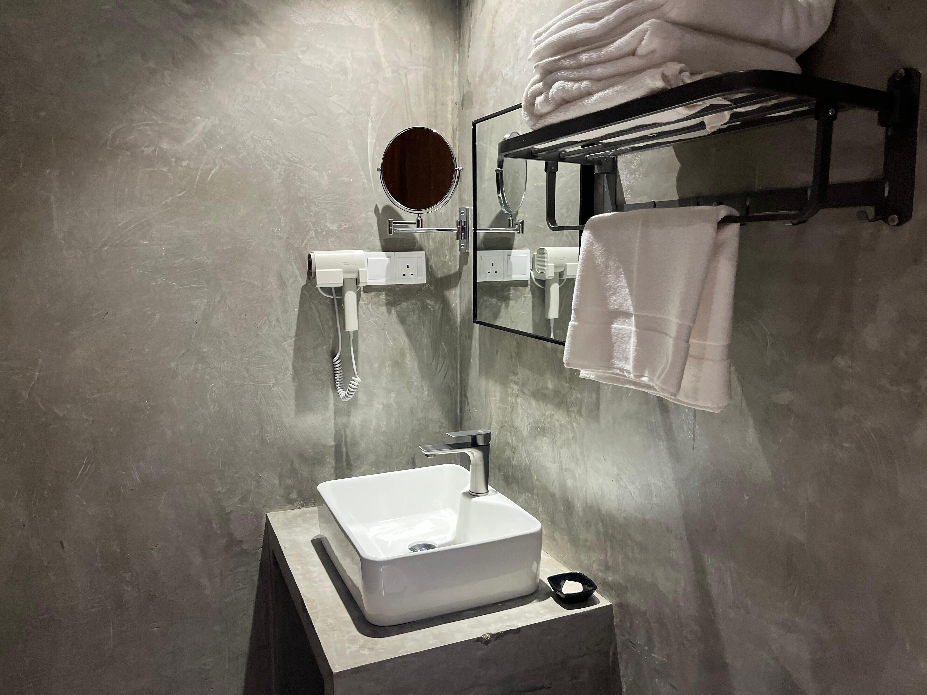 A modern bathroom with a white sink, a mirror, a towel rack, and a hairdryer.