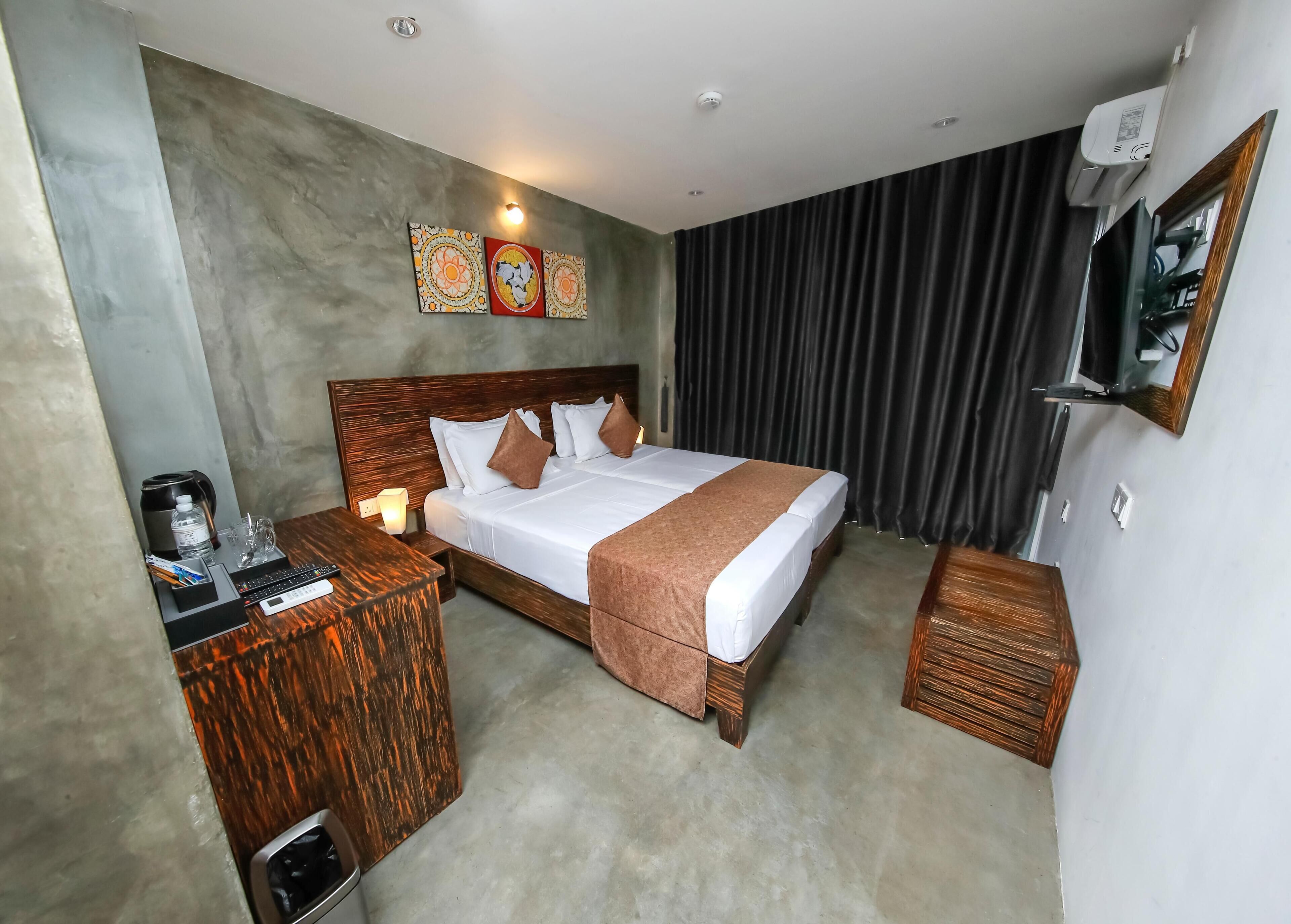Habitación de hotel con cama, mesita de noche, lámpara y televisor de pantalla plana montado en la pared.