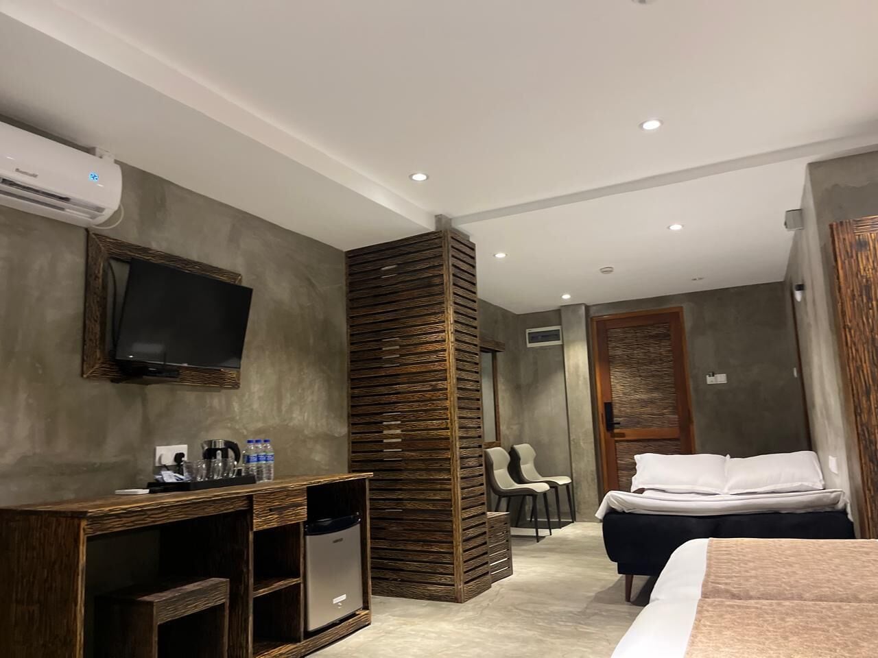 A hotel room with a bed, a desk with a television, a seating area with chairs, and a large pillar.