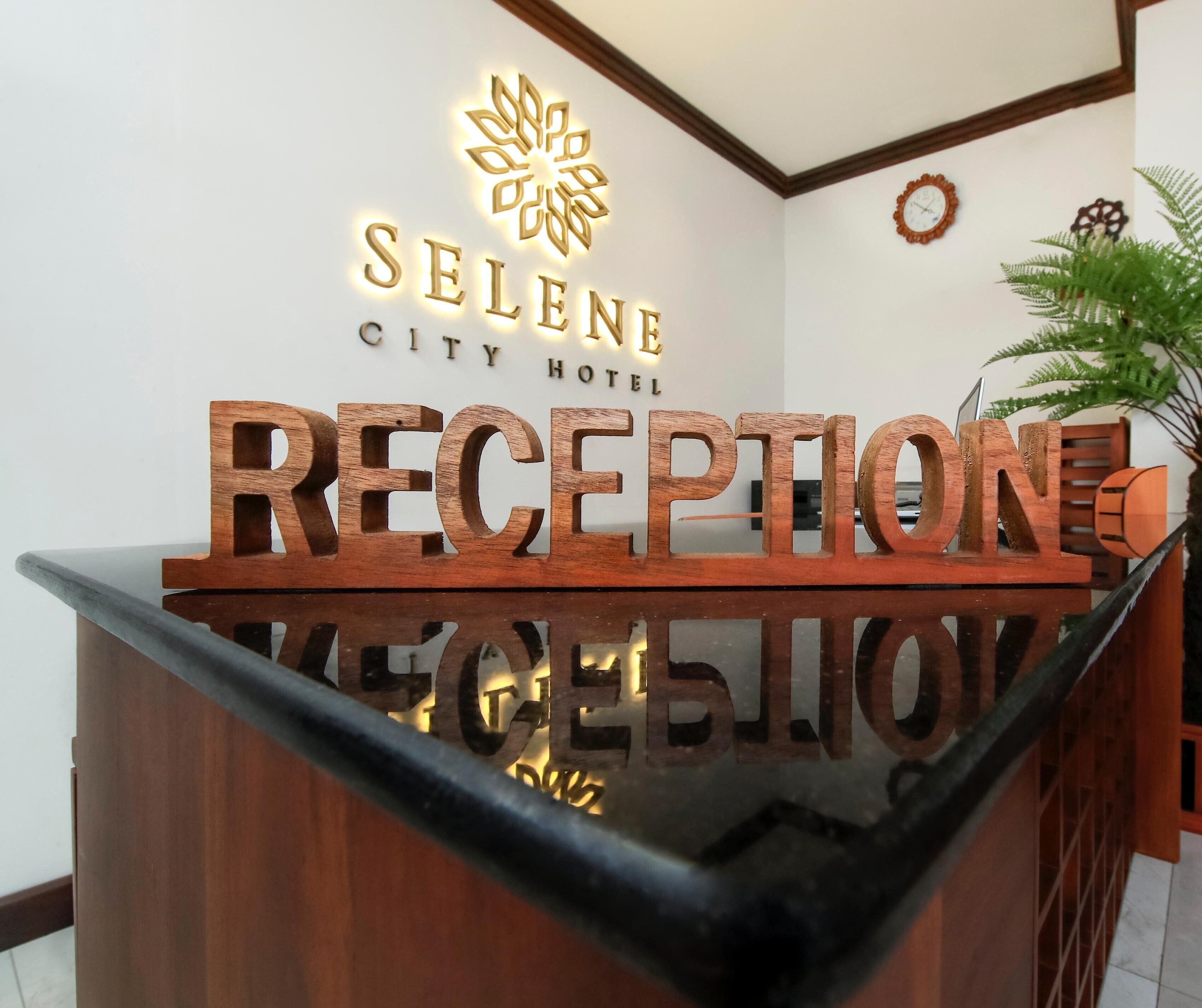 A reception desk with a wooden sign reading "RECEPTION" and "SELENE CITY HOTEL" above it.