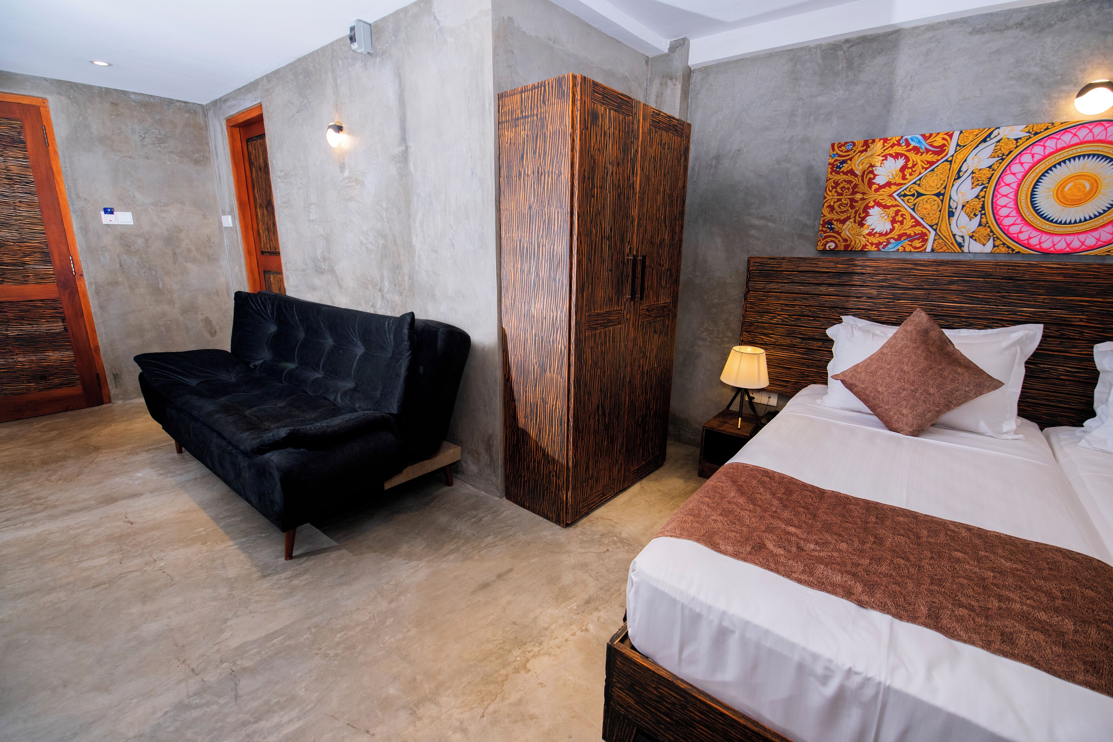 A hotel room with a bed, a sofa, a wardrobe, and a painting on the wall.