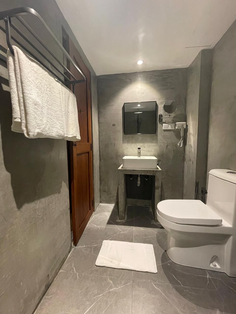 A bathroom with a marble floor, a white sink, a toilet, and a towel rack with towels.