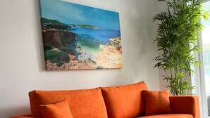 Ein modernes Wohnzimmer mit einer Couch, einem Glastisch, einem Gemälde einer Küstenlandschaft und einer Bambuspflanze.