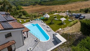 A pool area with lounge chairs and umbrellas, surrounded by a landscaped garden and a view of rolling hills and the sea. - Cosy apartment in villa for 4 people with A/C, WIFI, pool, TV, patio and pets allowed (Silvi)