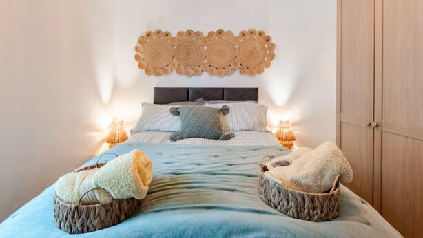 Ein Schlafzimmer mit einem Bett, zwei Nachttischlampen, einem Kopfteil mit dekorativer Applikation und einem Kleiderschrank.