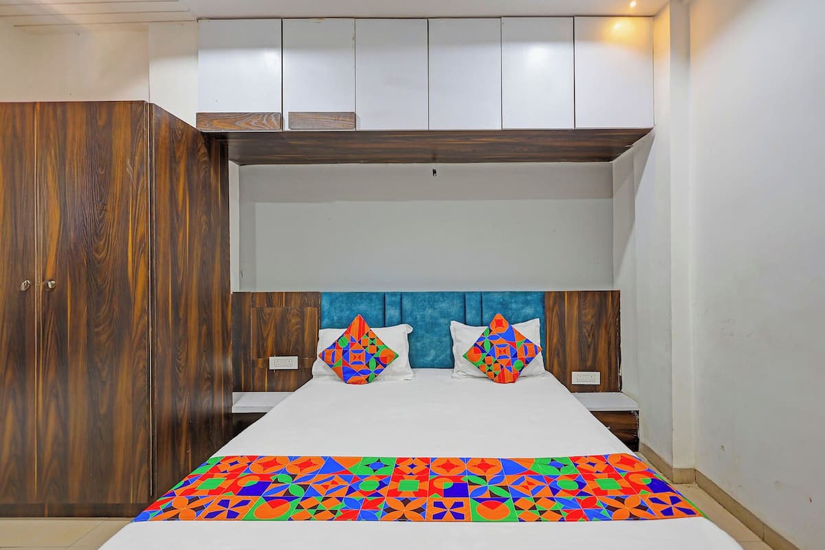 Une chambre avec une armoire en bois, un lit recouvert d’une courtepointe aux motifs géométriques colorés et une tête de lit bleue.