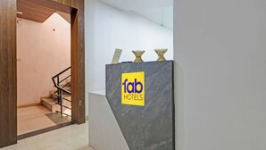 A hotel reception area with a modern design, featuring a marble reception desk and a staircase leading to an upper floor. - FabHotel Kas (Chhatrapati Sambhajinagar)