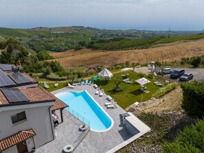 A pool area with lounge chairs and umbrellas, surrounded by a landscaped garden and a view of rolling hills and the sea. - Lovely apartment in villa with WIFI, A/C, hot tub, pool, TV, patio, pets allowed, panoramic view (Silvi)