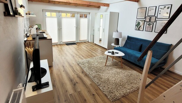 Un vaste espace de vie doté d’un plancher en bois, d’un canapé bleu, d’une table basse blanche et d’un escalier.