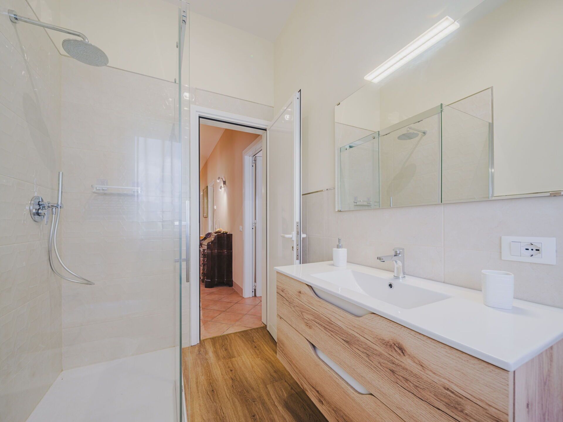 Un baño moderno con cabina de ducha de vidrio, tocador de madera y un espejo grande.