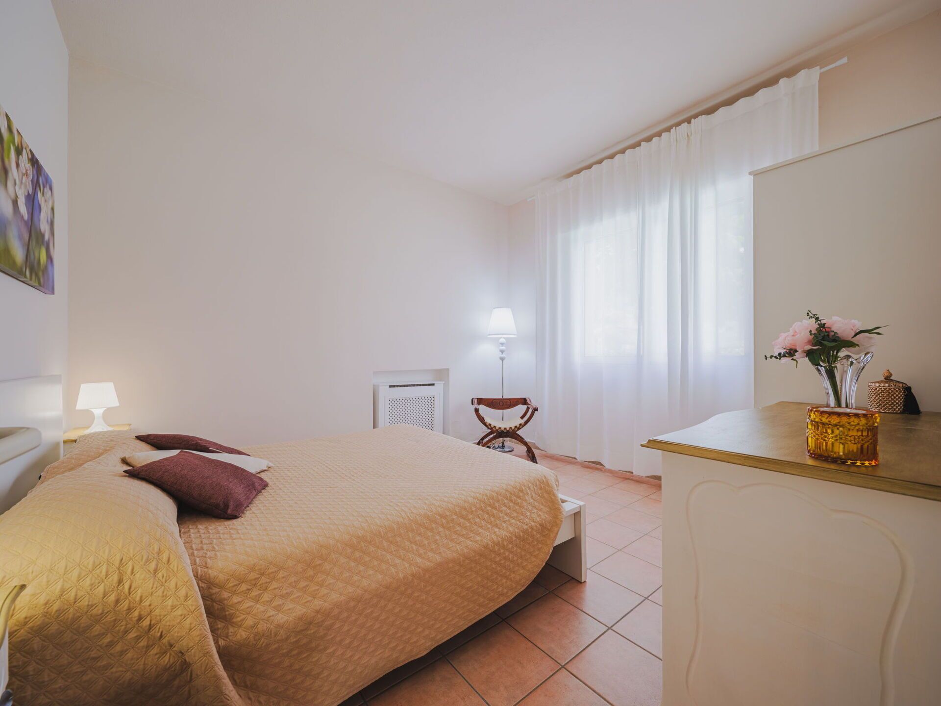 Een hotelkamer met een bed, nachtkastje, lamp, stoel en bureau met een bloevas.