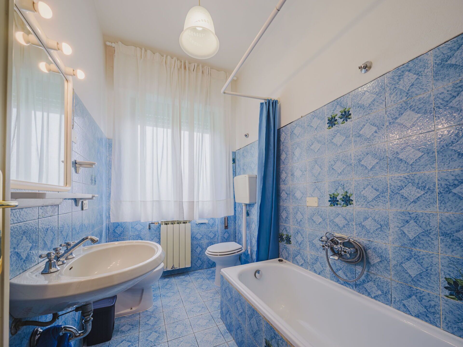 Une salle de bain équipée d’un lavabo, de toilettes et d’une baignoire, avec des carreaux bleus à motifs et un luminaire blanc au plafond.