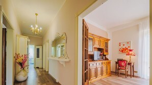 Un pasillo con piso de madera, un candelabro, un espejo y un mueble con televisor.