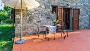Eine Terrasse im Freien mit einer Steinmauer, einem Tisch mit Stühlen, einer Topfpflanze und einem Sonnenschirm.