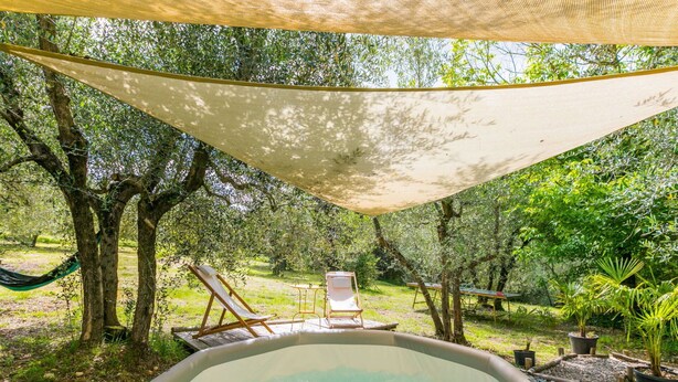 An outdoor hot tub area with lounge chairs and a canopy, surrounded by trees and greenery.