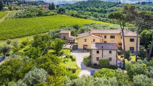 A large stone building with a yellow facade, surrounded by lush greenery and vineyards.