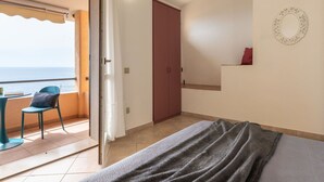 A bedroom with a bed, a chair, a small table, a wardrobe, and a view of the sea. - Cosy apartment for 4 guests with A/C, TV and patio (Villaputzu)