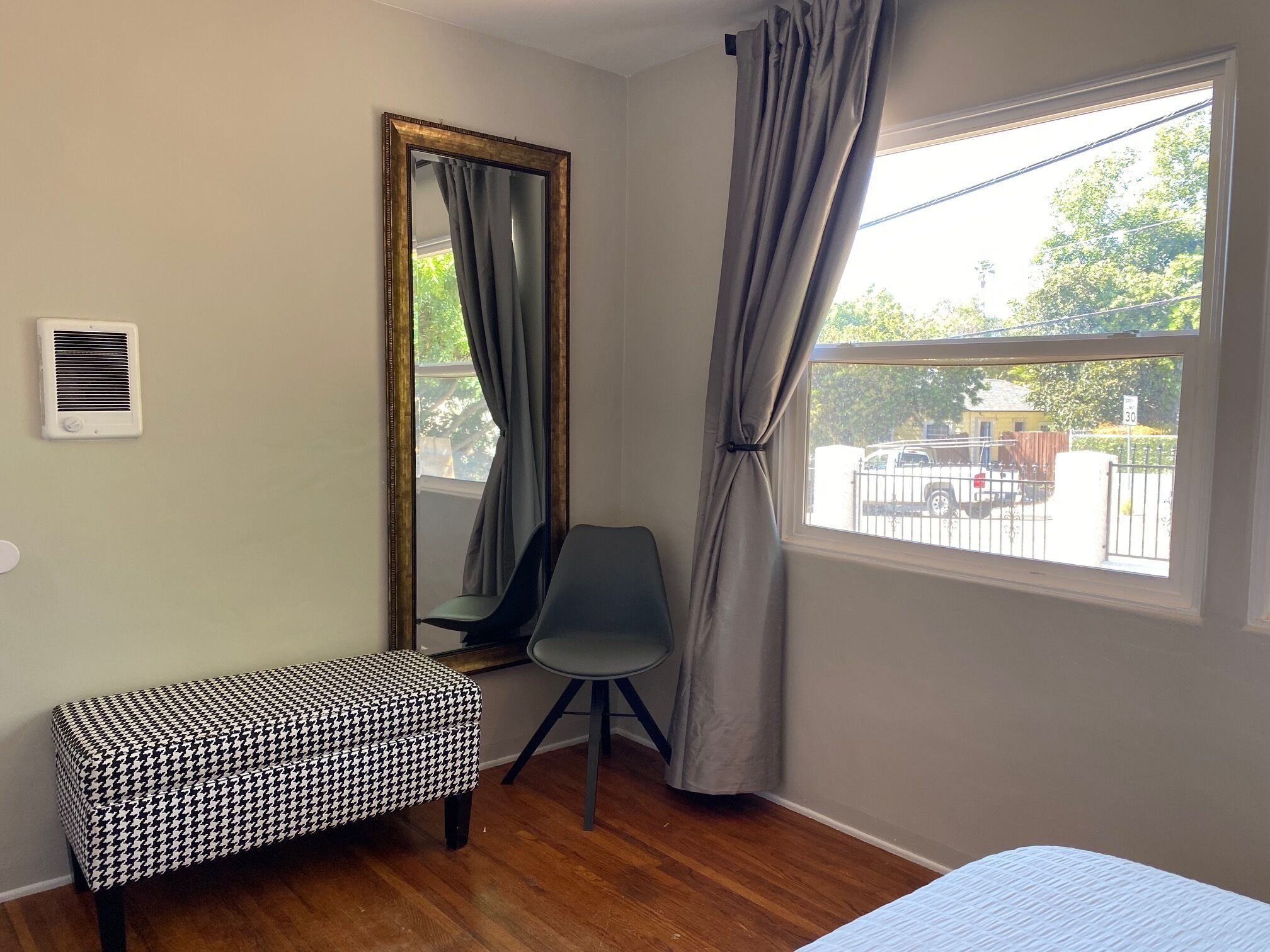 Ein Zimmer mit einer Sitzbank im Hundeohrenmuster, einem Sessel, einem großen Spiegel und einem Fenster mit Blick ins Freie.