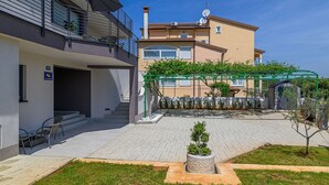 A modern apartment building with a covered outdoor area, a staircase, and a small garden.