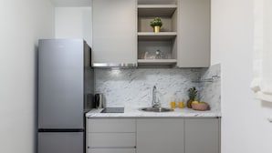 A compact kitchen with a stainless steel refrigerator, a built-in sink, and a marble backsplash.