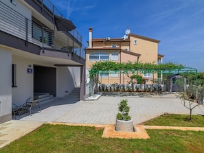 A modern apartment building with a covered outdoor area, a staircase, and a small garden.