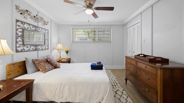 Une chambre à coucher comprenant un lit, une commode, une table de chevet et un ventilateur de plafond.