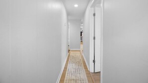 Un couloir étroit aux murs blancs et au plancher en bois.