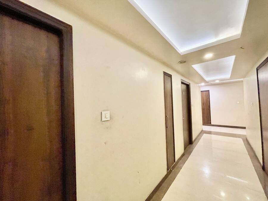 A hotel corridor with a modern ceiling design, wooden doors, and a clean, tiled floor.