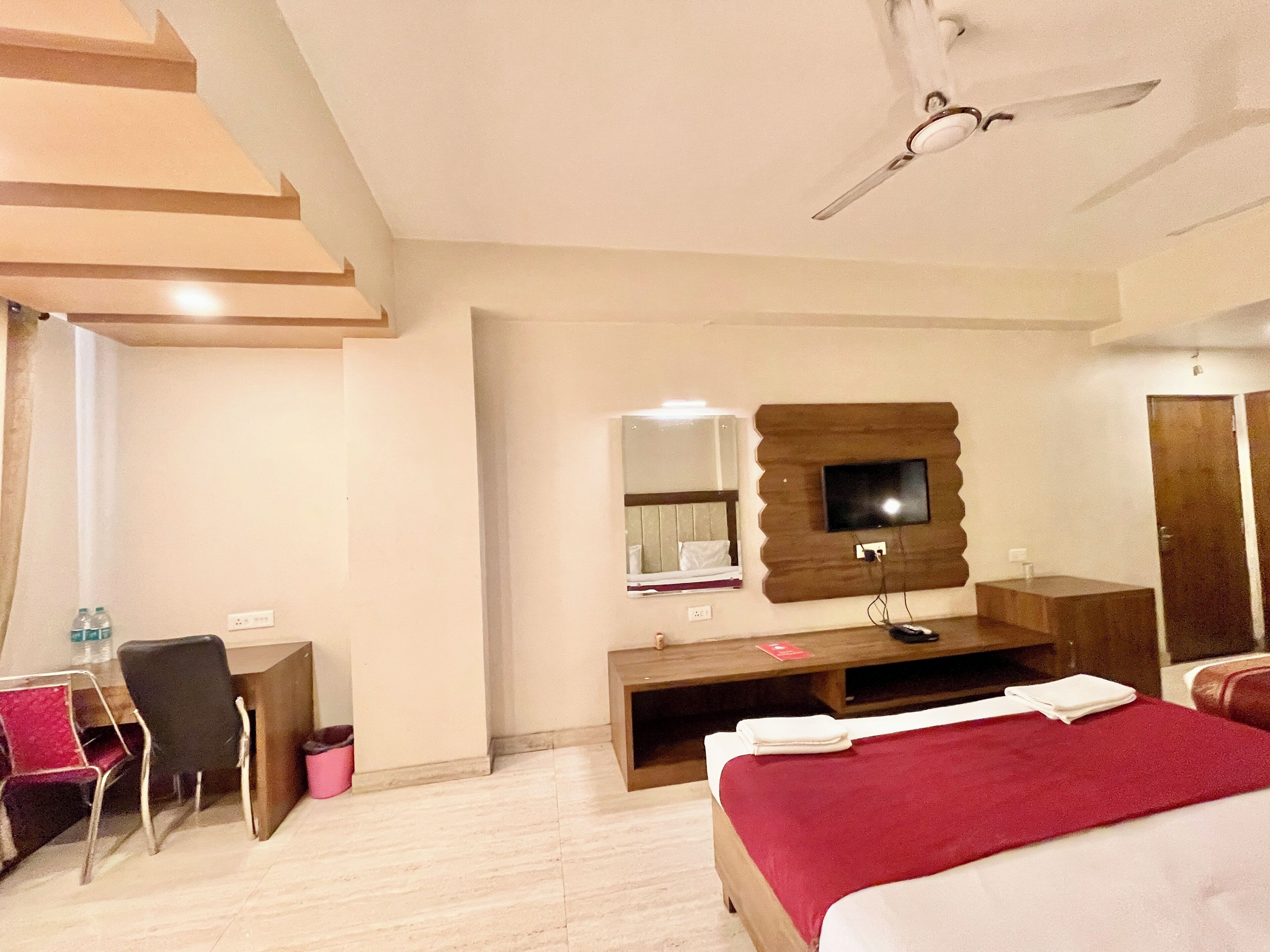 Ein Hotelzimmer mit einem Bett, einem Schreibtisch, einem Sessel, einem an der Wand befestigten Fernseher und einem Deckenventilator.