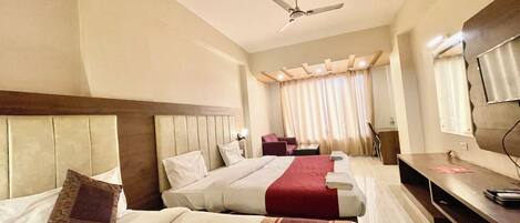 Ein Hotelzimmer mit zwei Betten, einem Schreibtisch, einem Stuhl, einem Fernseher und einem Deckenventilator.