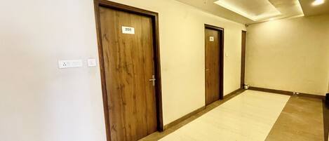 Un couloir avec trois portes en bois, chacune portant un numéro. Les murs sont unis et le sol est carrelé.