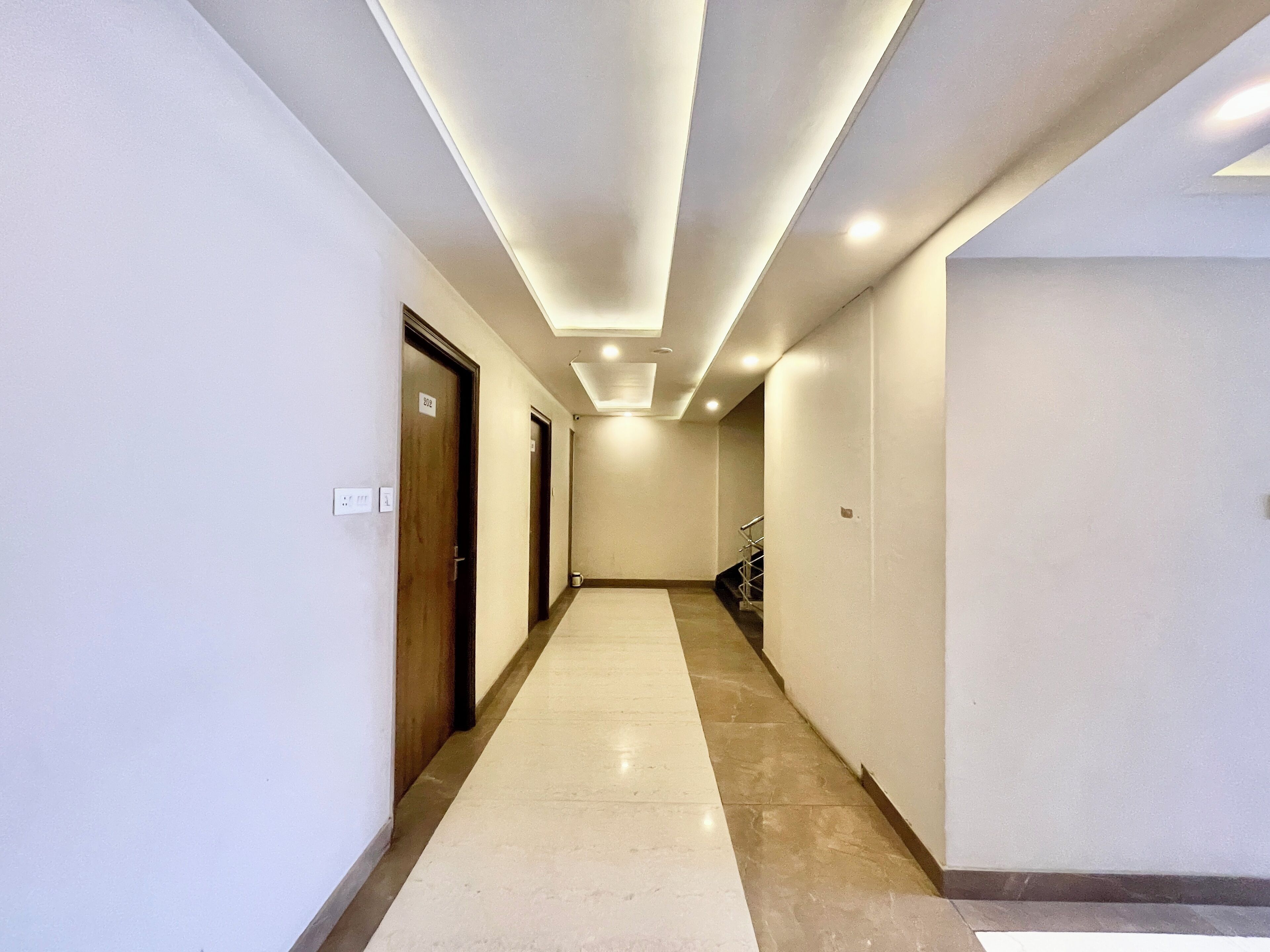 Un pasillo con suelo de baldosas, una escalera a la derecha y puertas a la izquierda.