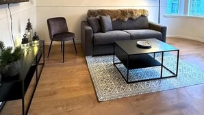 Een moderne woonkamer met een grijze bank, een zwarte salontafel en een vloerkleed met dessin.